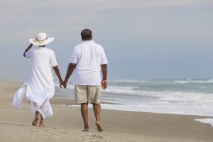 Happy romantic senior African American man and woman couple walking holding hands on a deserted tropical beach