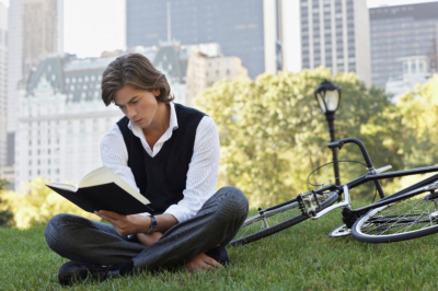 Young man sitting cross legged in a park and reading a book.