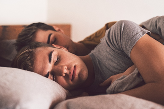 Two men spooning in bed, sleeping.